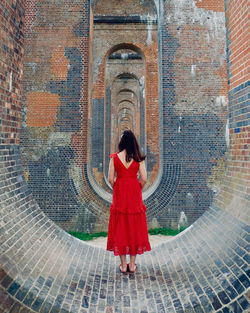 Full length rear view of woman standing against brick wall