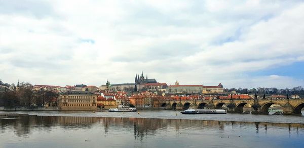 Bridge over river by buildings against sky