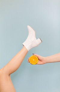 Cropped image of woman holding orange against blue background