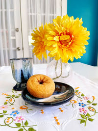 Close-up pottery cup saucer with doughnut,  flowers in glass vase, embroidery, still life