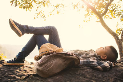 Side view of boy lying on fallen tree against sky