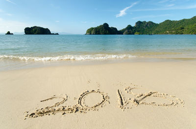 Text on sand at beach against sky