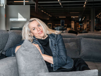 Joyful silver-haired lady in a dark denim jacket nestled on a charcoal sofa