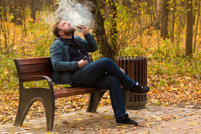 Man smoking pipe while sitting on bench during autumn