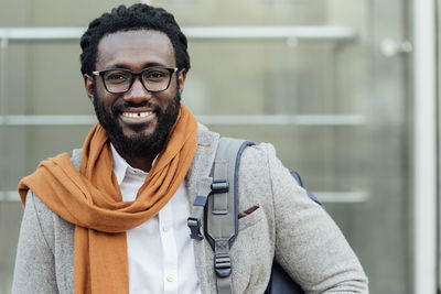 Portrait of smiling young man with backpack standing in city