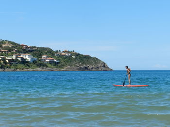 Full length side view of woman paddleboarding in sea against blue sky