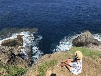 High angle view of woman sitting on cliff by sea