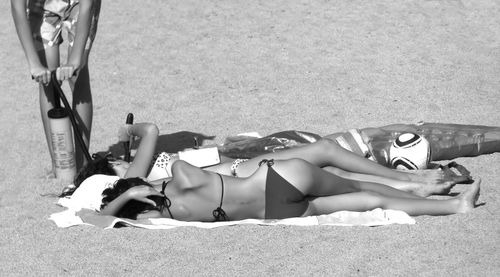 Women in bikini relaxing on sand at beach during sunny day