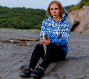 Portrait of young woman with insulated drink container sitting at beach