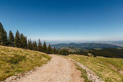 Dirt road along landscape against clear blue sky