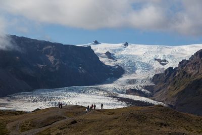 Mid distance view people on snowcapped mountain against cloudy sky