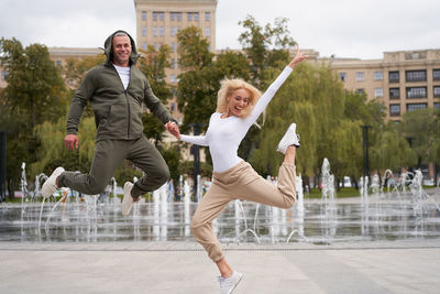 Full length of couple jumping against fountain