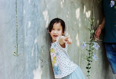 Portrait of smiling girl pointing while standing against wall