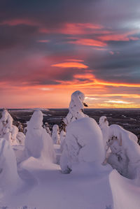 Snow covered land against sky during sunset