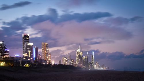 Illuminated buildings by sea against sky at night