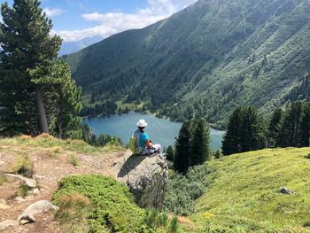 Rear view of woman looking at river and mountain while sitting on rock