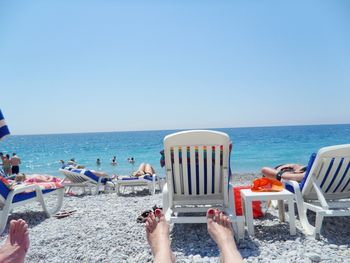 People relaxing on lounge chairs at beach against clear sky on sunny day