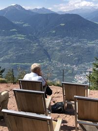 Rear view of woman sitting on shore against mountains