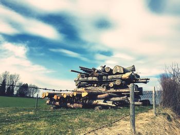 Stack of logs on field against sky