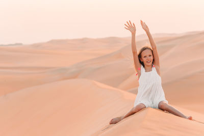Young woman with arms raised on sand in desert