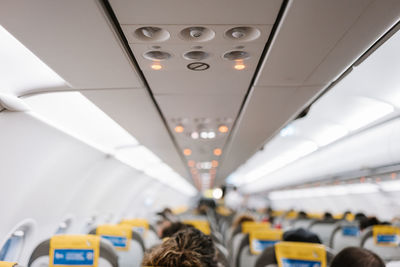 Unrecognizable passengers sitting on comfortable chairs under control panel inside contemporary aircraft during trip