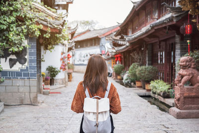 Rear view of backpack woman standing amidst building in town