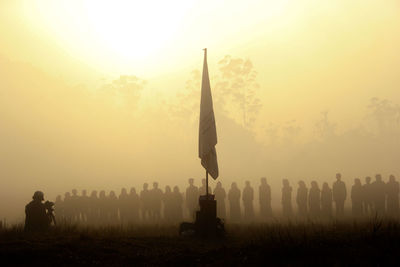 Silhouette people by flag against sky during sunset