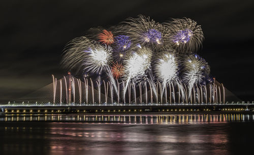 Firework display over river against sky at night