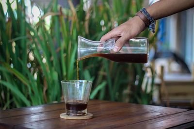 Close-up of hand pouring drink in glass on table