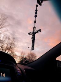 Close-up of rosary hanging in car against sky during sunset