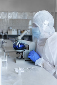 Woman scientist wearing protective costume, screen, gloves working in laboratory making a covid test