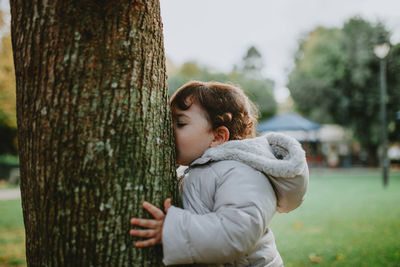 Side view of baby girl kissing tree trunk