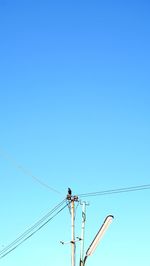 Low angle view of electricity pylon against clear blue sky