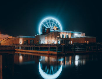 Illuminated ferris wheel in city against sky at night