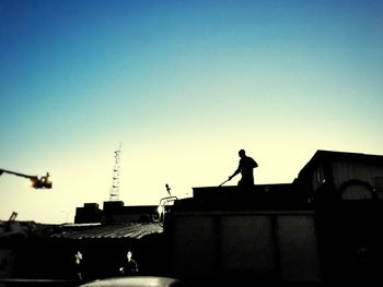 Silhouette man standing by statue in city against clear sky