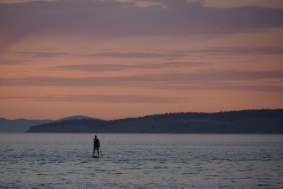 Silhouette man paddleboarding in lake against sky during sunset