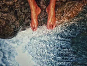 Low section of person sitting on rock by sea