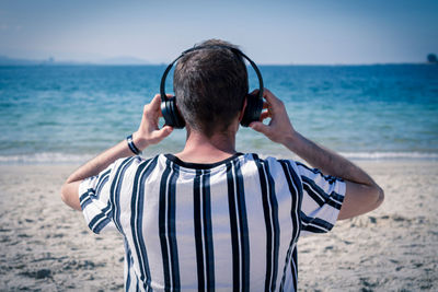 Rear view of man standing at beach against sky