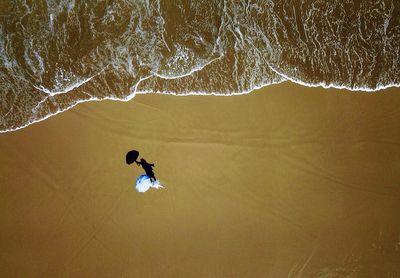 Aerial view of woman with umbrella standing at sandy beach
