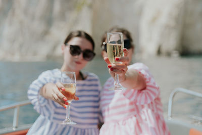 Portrait of caucasian beautiful girls in sunglasses sitting in a boat holding glasses of champagne