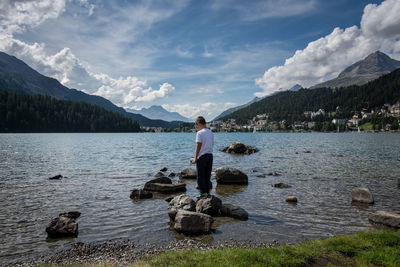 Rear view of boy standing on rock in lake against sky