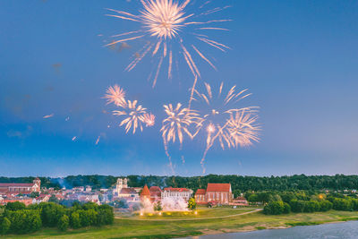 Firework display by building against blue sky