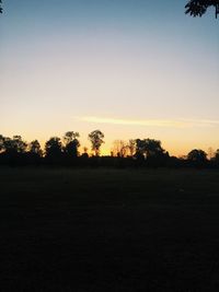 Silhouette trees on field against clear sky