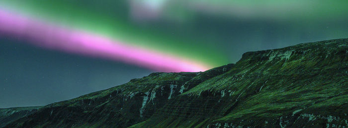 Low angle view of aurora over mountain against sky