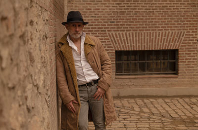 Portrait of adult man in hat and coat against brick wall on street. madrid, spain