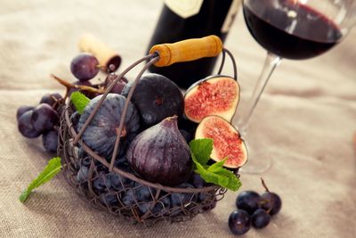 High angle view of figs and grapes in basket by red wine on table