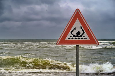 Warning sign on sea against sky