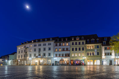 Buildings by street against blue sky at night