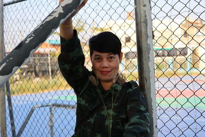 Portrait of smiling woman standing against chainlink fence