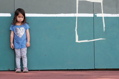 Full length portrait of girl standing against wall